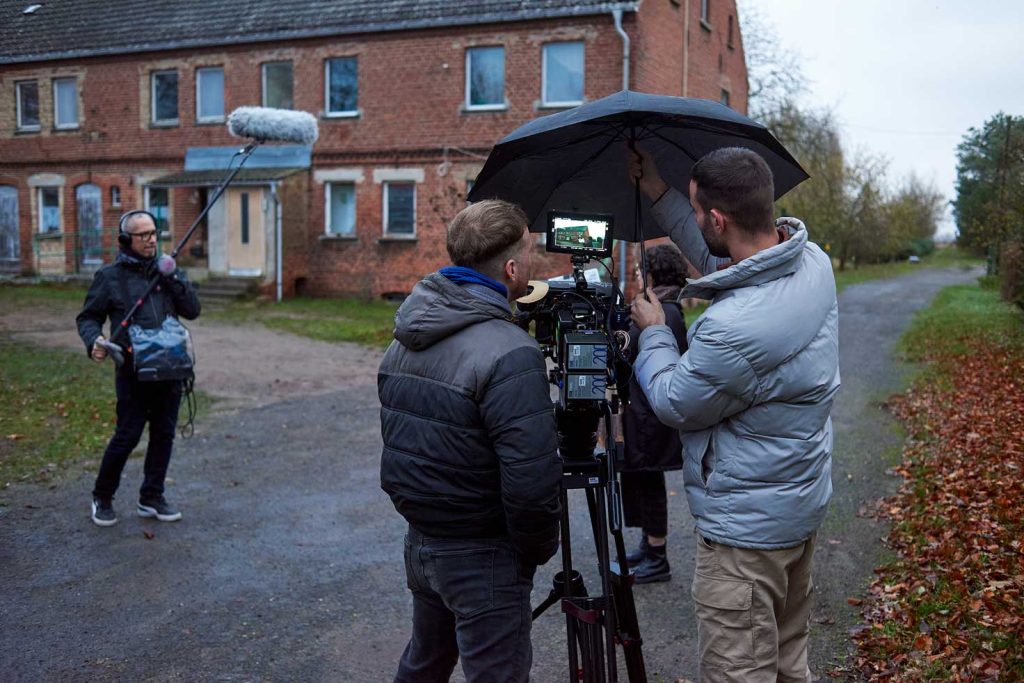 Queer cinema behind the scenes image of film crew setting up an outdoor shoot in rainy weather