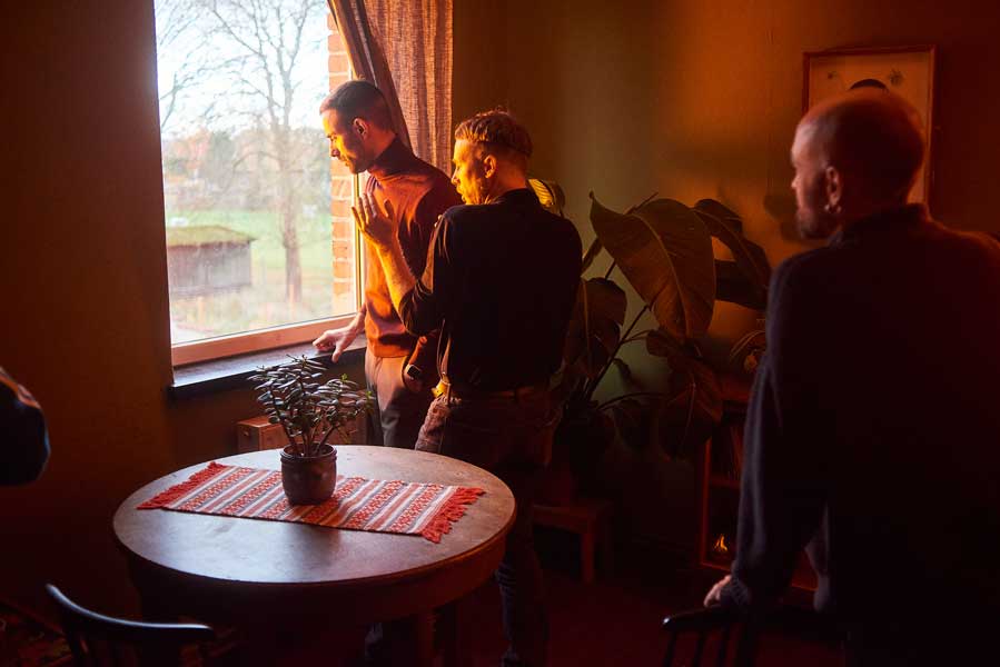 Queer cinema behind the scenes image of director and performers preparing a scene beside a window in warm interior light